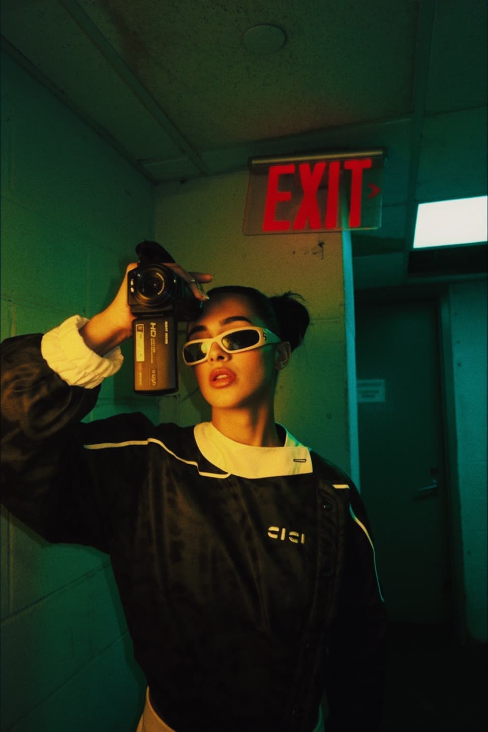 CICIBI with a camcorder under a green EXIT sign